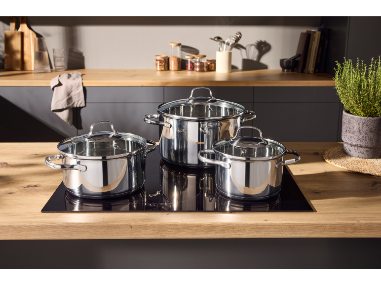 Drie glanzende kookpannen met glazen deksels op een kookplaat in een moderne keuken.