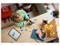 Een kind bouwt een LEGO-robot op een houten tafel, met een tablet die instructies toont.
