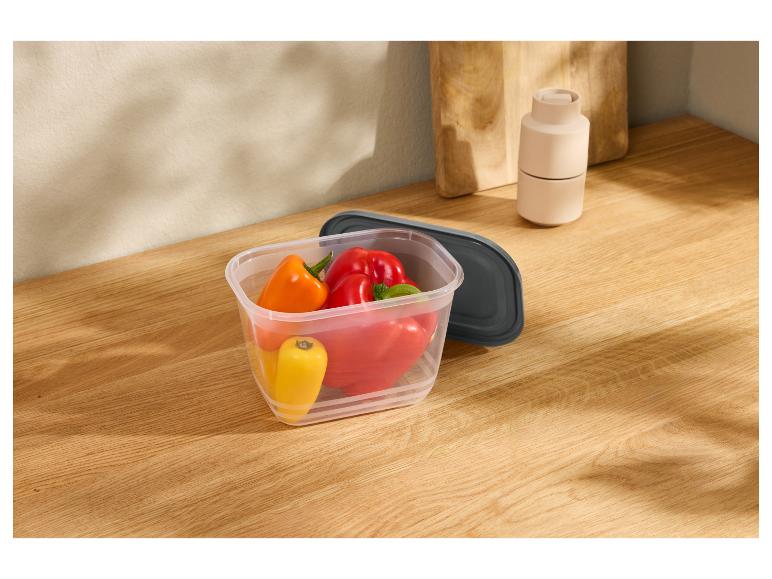 Paprika's in plastic bewaarbak met donkergrijs deksel op een houten aanrecht.