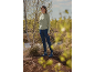 Vrouw in groene trui, donkerblauwe jeans en blauwe laarzen staat in de natuur.