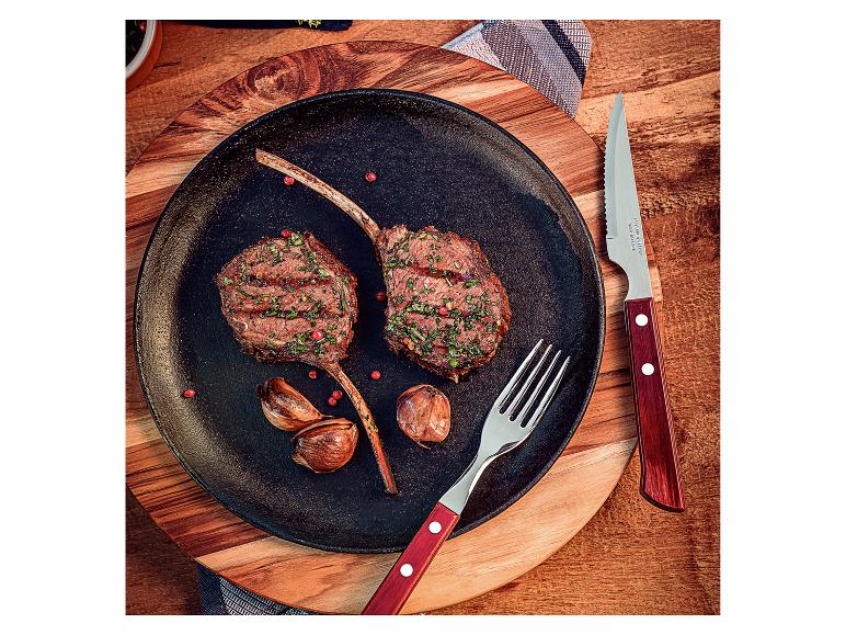 Twee gegrilde lamskoteletten met knoflook en bestek op een houten plank.