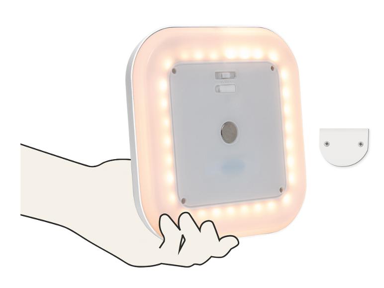 Vierkante LED-lamp met warm wit licht, vastgehouden door een hand, met een montagebeugel ernaast.