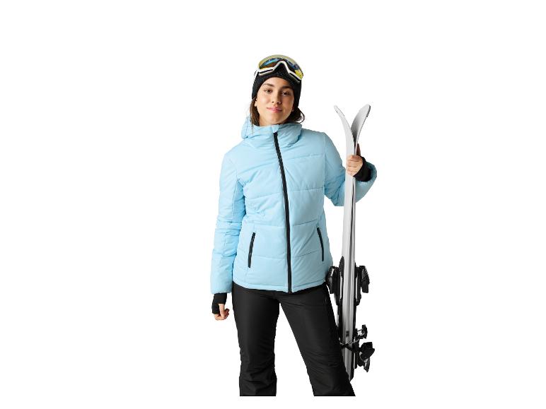 Een vrouw in een lichtblauwe ski-jas en zwarte skibroek met ski's.