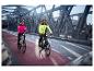 Twee fietsers in CRIVIT thermo-hybrid jassen op een brug, één in roze, één in neongeel.
