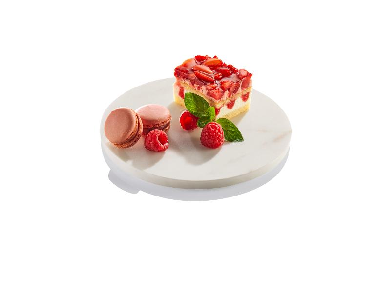 Een stukje taart met aardbeien, macarons en frambozen op een marmeren onderstel.