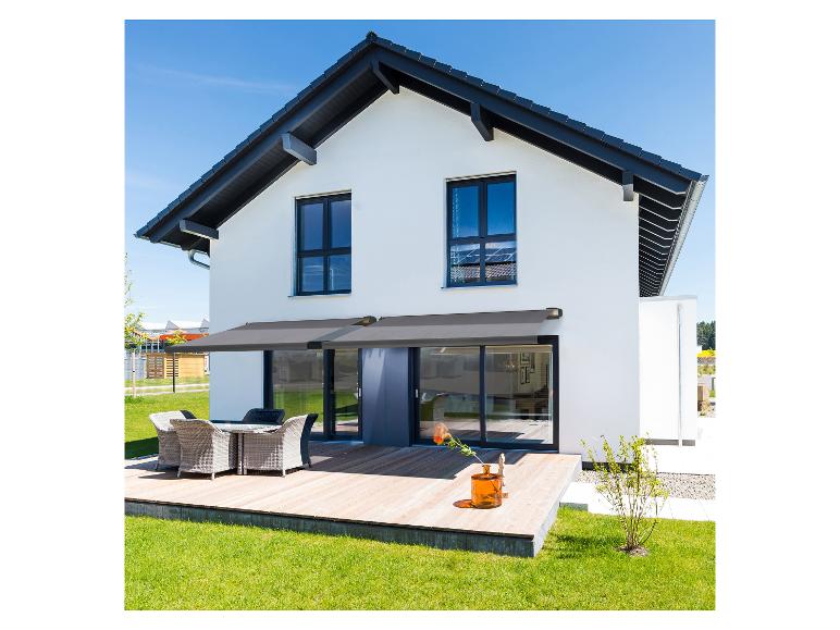 Modern huis met grijs zonnescherm boven houten terras en tuinmeubelen.