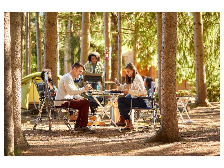 Een groep mensen geniet van een maaltijd aan een opklapbare tafel in het bos.