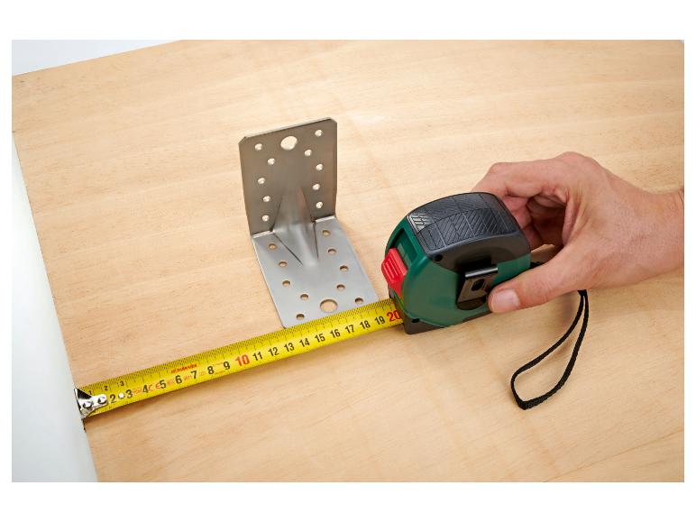 Een houten plank meten met een meetlint naast een metalen beugel.