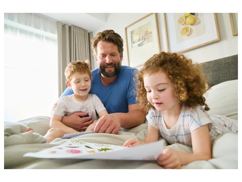 Vader en kinderen lezen een prentenboek in bed.