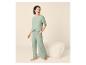 Vrouw in lichtgroene pyjama met broek en T-shirt, staand naast een poef.