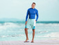 Man in blauwe rashguard en blauwe zwembroek met 'mi' logo op het strand.