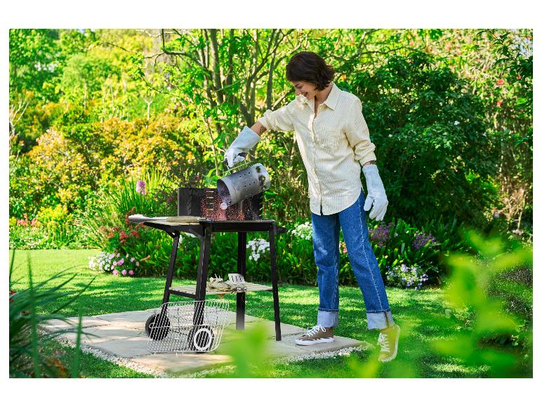 Vrouw giet gloeiende kolen uit een brikettenstarter in een barbecue in de tuin.