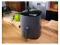 Een grijze airfryer op een houten aanrecht, met groenten op de achtergrond.