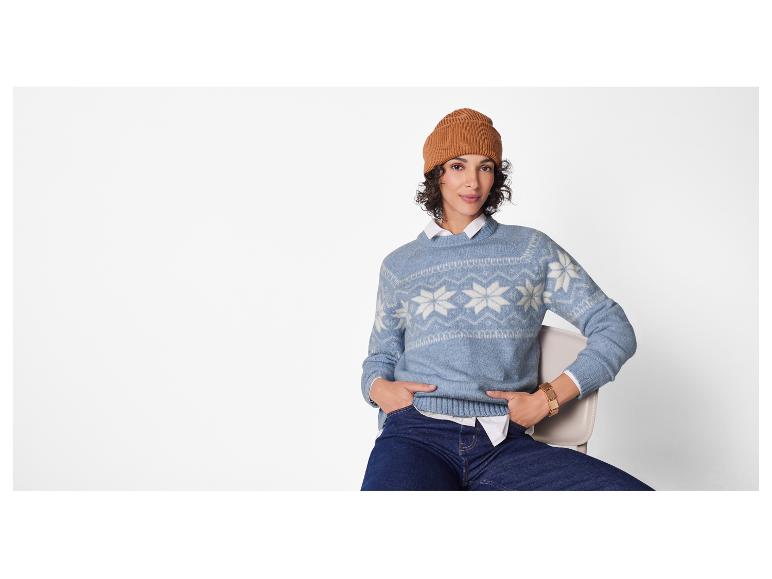 Een vrouw in een blauwe Fair Isle trui, wit overhemd en jeans, met een bruine muts.