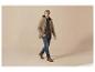 Man in beige jas, geruit overhemd, jeans en bruine schoenen, lopend.