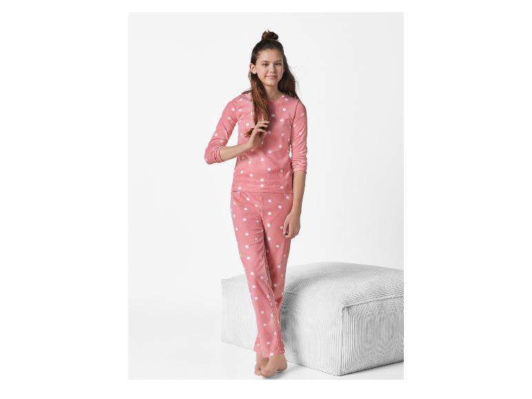 Meisje in roze pyjama met witte stippen, naast een witte poef.