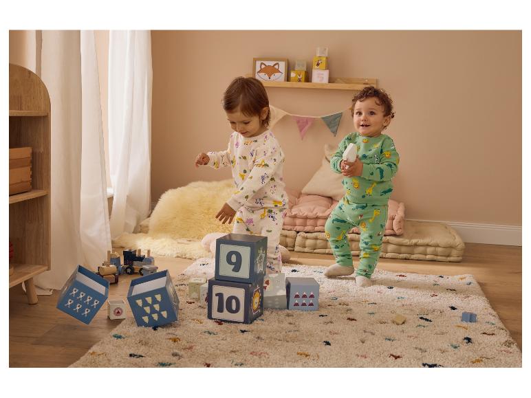 Twee peuters in dierenpyjama's, spelend met blokken en een houten trein op een vloerkleed.