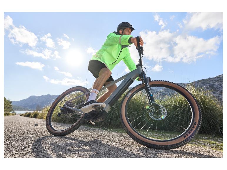 Een man in een neon groene jas rijdt op een Maxxis e-bike over een grindweg.