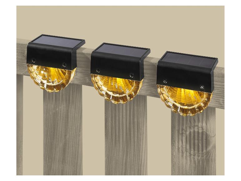 Drie solar schuttinglampen met warm geel licht bevestigd aan een houten schutting.