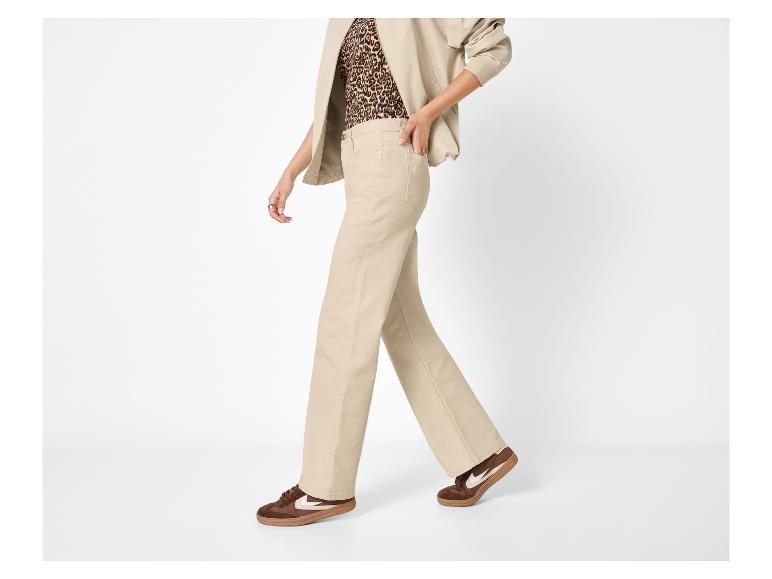 Vrouw in beige wijde broek, top met luipaardprint en bruine sneakers.