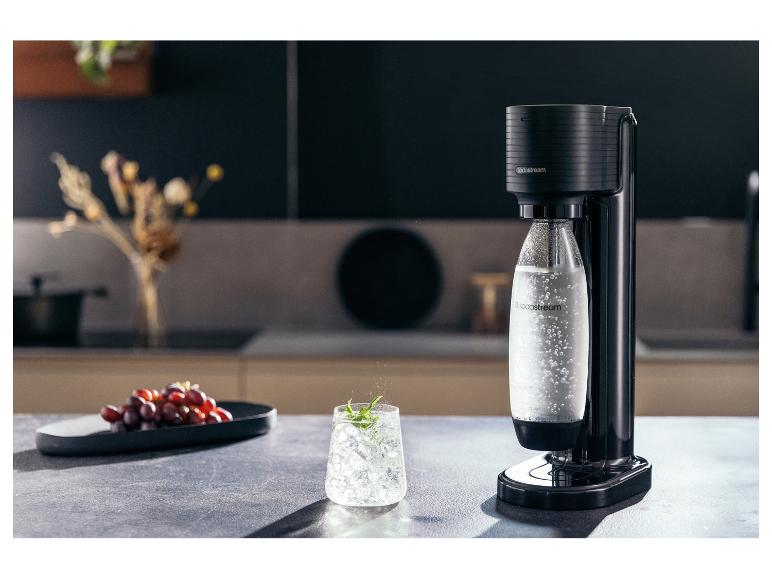 Bruiswatermaker met een fles bruiswater, een glas ijswater en druiven.