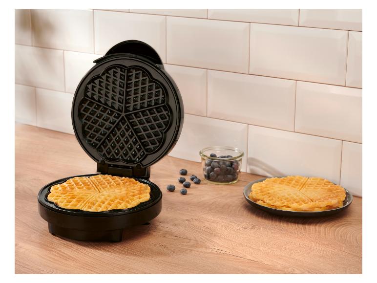 Open wafelijzer met een versgebakken wafel, bosbessen en wafels op een bord.