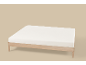 Licht houten bed met een wit matras op een beige achtergrond.