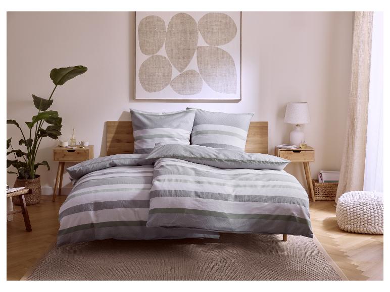 Slaapkamer met grijsgroen gestreept beddengoed, houten nachtkastjes en een grote plant.