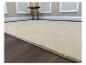Beige vloerkleed op een donkere houten vloer, met een bijzettafeltje op de achtergrond.
