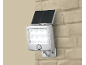 Zilverkleurige LED-zonnelamp met bewegingssensor, gemonteerd op een beige bakstenen muur.