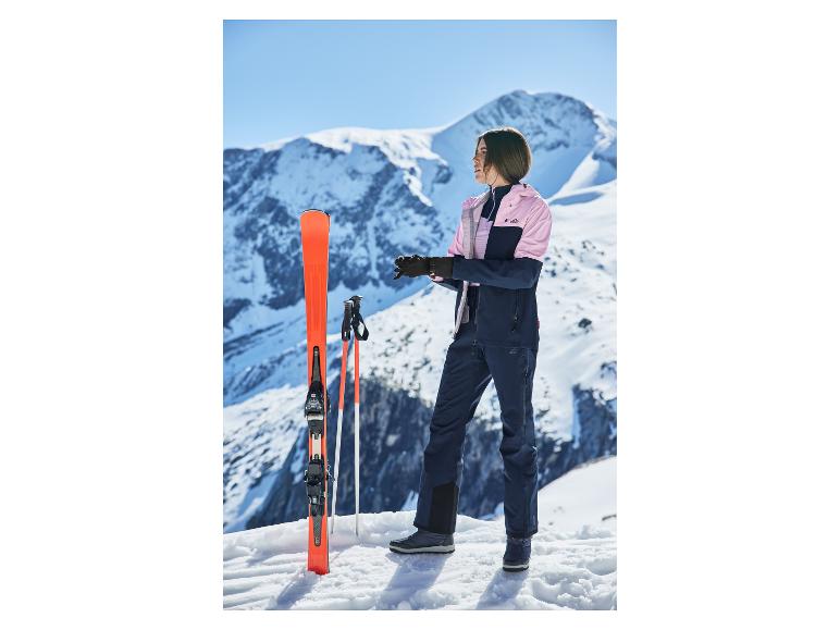 Vrouw in ski-jas en -broek, met ski's en stokken, op een besneeuwde berg.