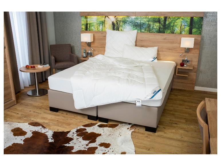 Slaapkamer met BeCo beddengoed, houten meubels en een koeienhuid vloerkleed.