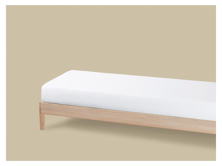 Een eenvoudig licht houten bed met een wit matras op een beige achtergrond.