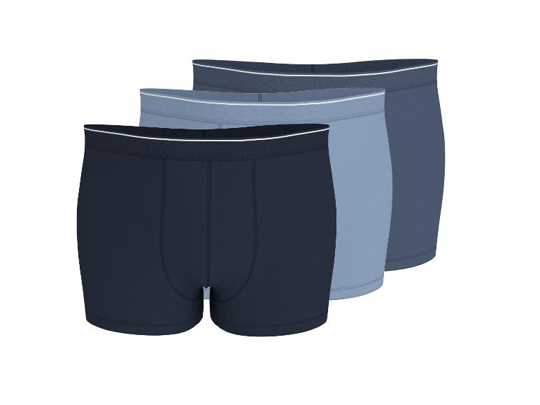 Drie paar herenboxershorts in blauwtinten, diagonaal gerangschikt.