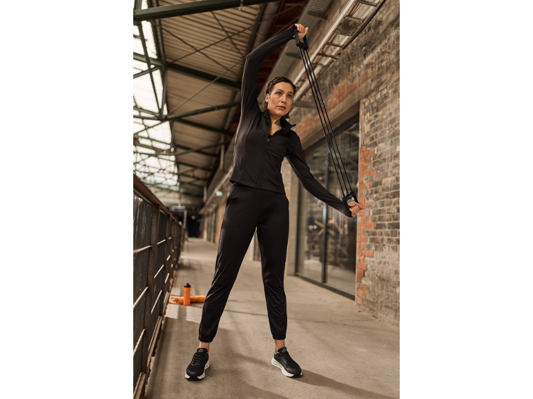 Vrouw in zwart sportpak traint buiten met een weerstandsband.