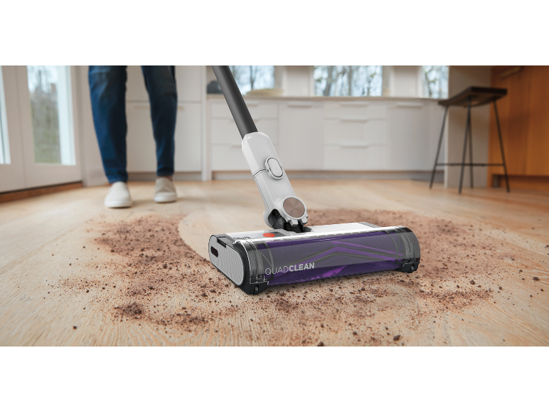 Draadloze stofzuiger reinigt gemorst vuil op een houten vloer in een keuken.