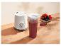 Witte persoonlijke blender met rode fruitsmoothie en een kom bessen op een houten tafel.