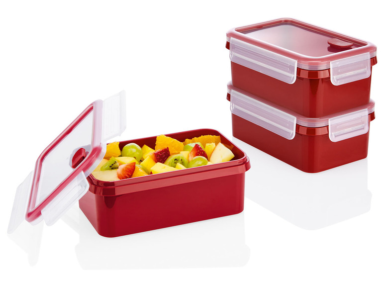 Drie rode plastic lunchboxen met fruit.
