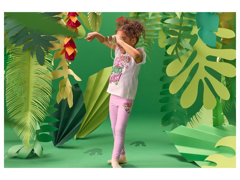 Meisje in jungle-setting, draagt een wit T-shirt en roze legging, kijkt door een verrekijker.