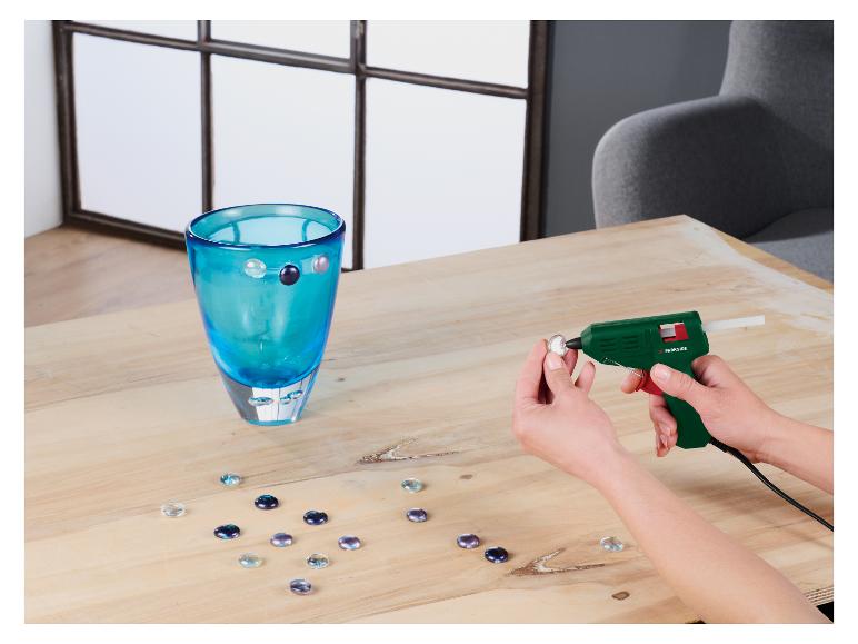 Een persoon versiert een turquoise vaas met glazen stenen met een lijmpistool.