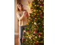 Vrouw versiert een kerstboom met rode en gouden kerstballen en warme lichtjes.