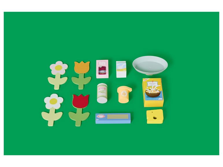 Houten speelgoed, waaronder bloemen, melk- en ontbijtgranendozen, en een bord, op een groene achtergrond.