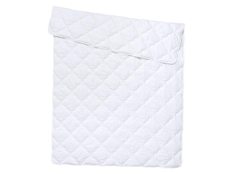 Wit, gewatteerd dekbed of matrasbeschermer opgevouwen op een witte achtergrond.