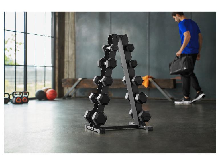 Een sportschool met een halterrek, kettlebells en ballen, met een man die een sporttas draagt.