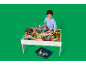 Kind speelt met een houten speeltafel met treinbaan en accessoires.