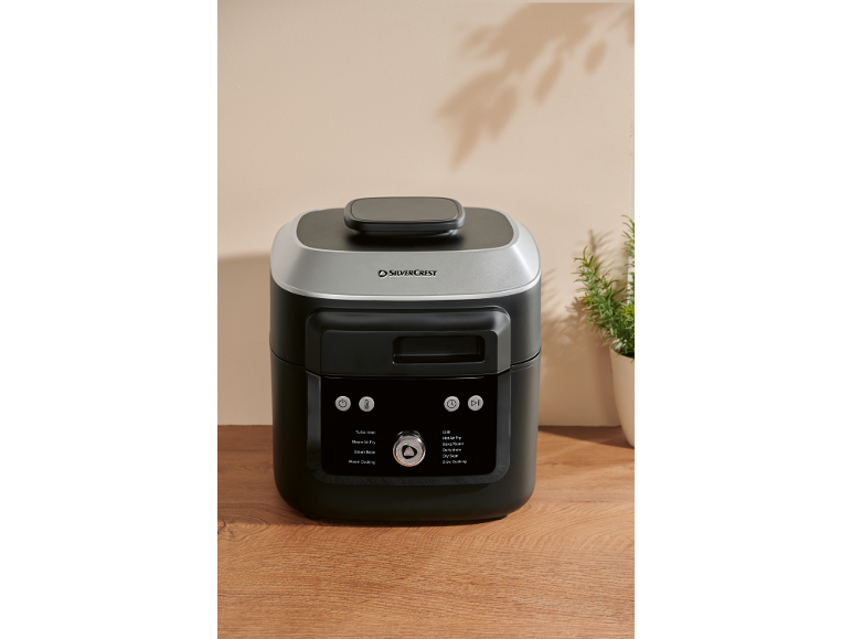 Zwarte en zilveren multicooker met diverse kookfuncties op een houten ondergrond.