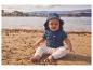 Baby in katoenen hoed en T-shirt op het strand.