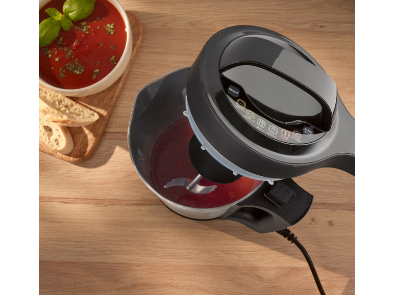 Een automatische soepmaker met rode soep en brood op een houten tafel.