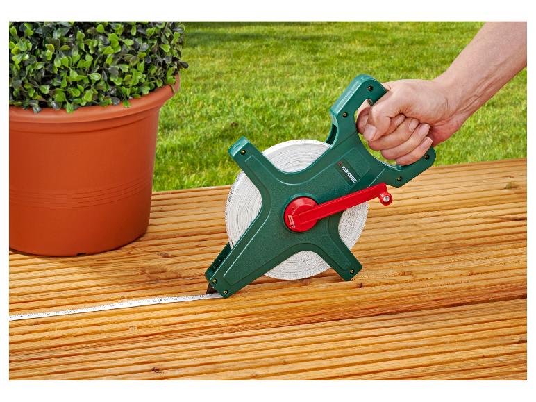 Hand houdt een meetlint vast op een houten terras naast een potplant.