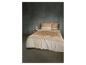 Beige en wit beddengoed met geometrische patronen op een bed met een nachtkastje en lamp.